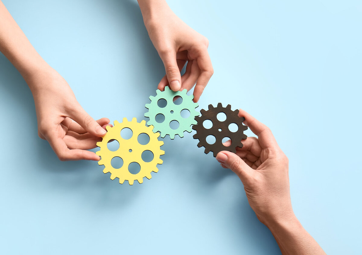 Three hands bring together differently colored gears. The interlocking gears symbolize collaboration, connectivity, and seamless digital processes.