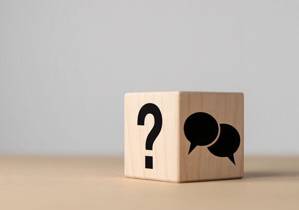 Holzw&uuml;rfel mit Fragezeichen und Sprechblasen-Symbol auf einem Tisch. Die Darstellung steht f&uuml;r h&auml;ufig gestellte Fragen, Informationen und Support.