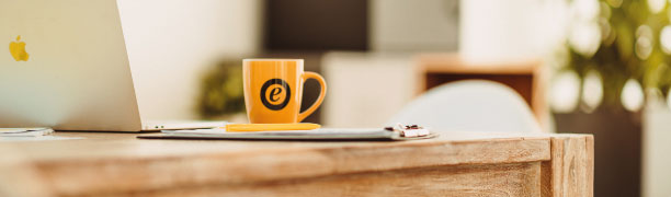 Close-up of a desk featuring an orange mug printed with the Trusted Shops GmbH logo.