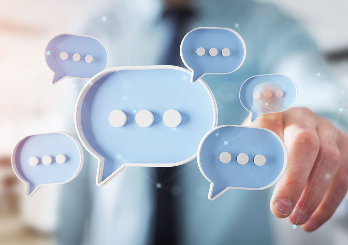 Digitala pratbubblor framf&ouml;r en person som pekar p&aring; ett virtuellt chattgr&auml;nssnitt, vilket symboliserar kommunikation, meddelandeutbyte och samarbete.