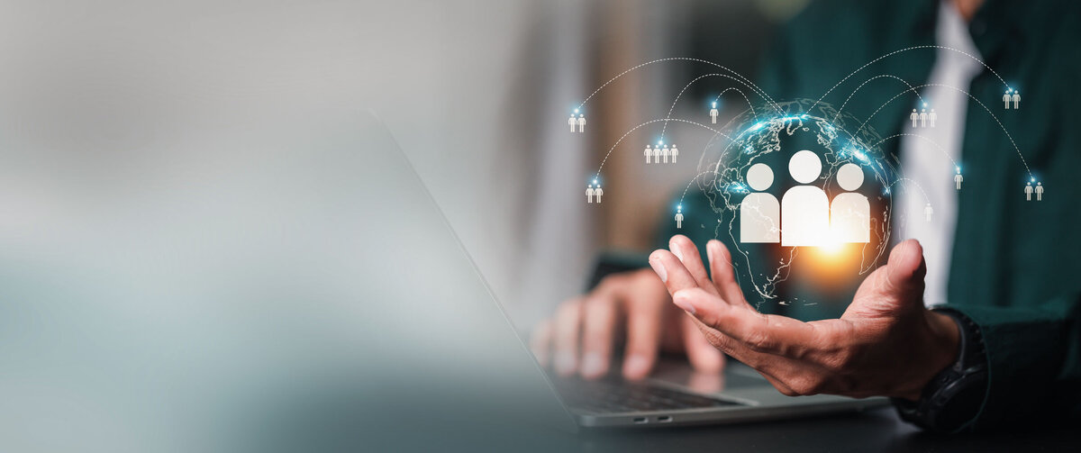 Persoon werkt op een laptop terwijl deze een digitale wereldbol vasthoudt met verbonden pictogrammen van personen. De afbeelding symboliseert digitale werving, HR-dienstverlening, talentmanagement en de wereldwijde verbondenheid van medewerkers en organisaties.