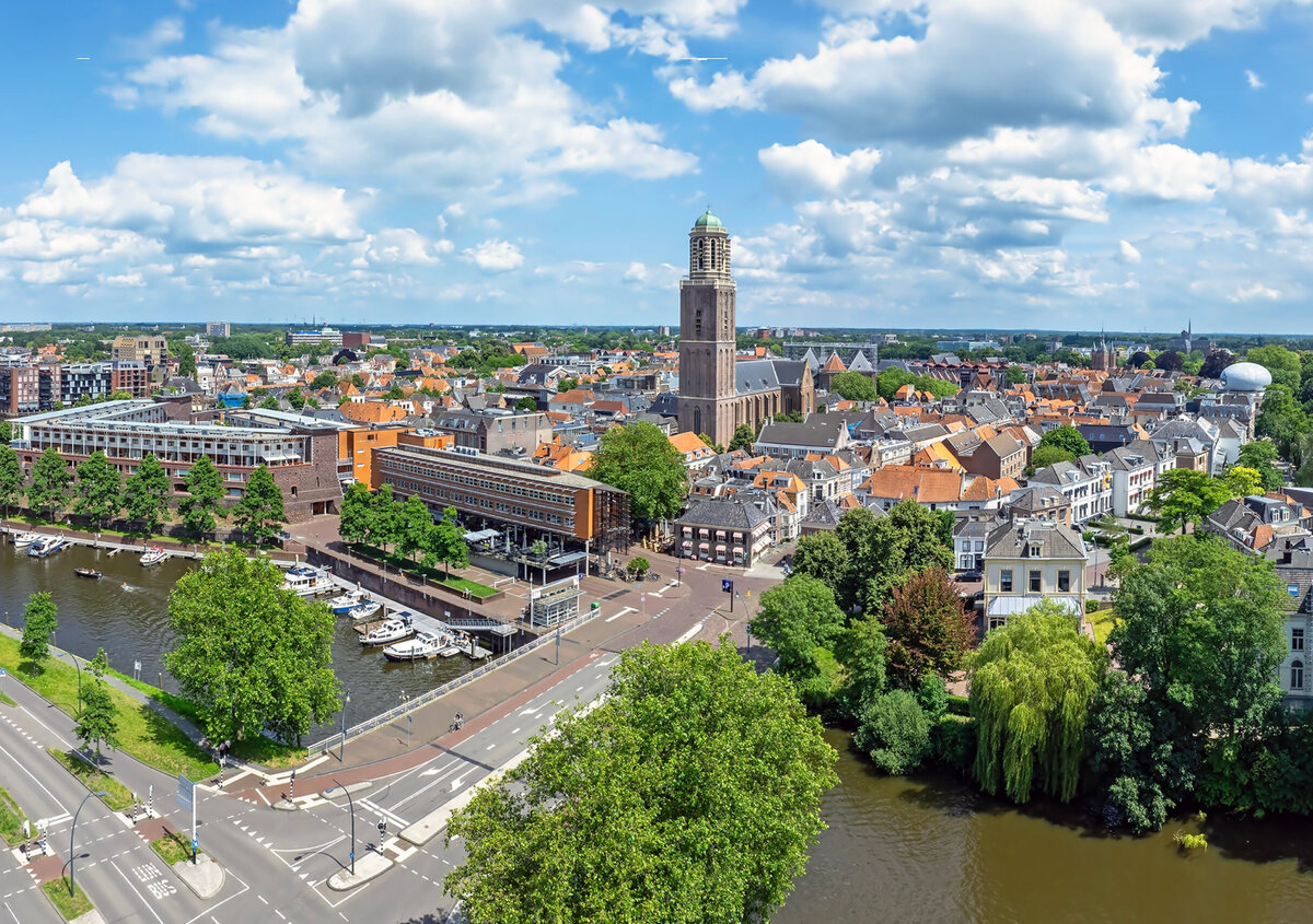 Flygvy &ouml;ver Zwolles historiska stadsk&auml;rna med byggnader med r&ouml;da tak, ett framtr&auml;dande kyrktorn, kanaler och en strandpromenad kantad av b&aring;tar. T&auml;ta stadskvarter och traditionell arkitektur dominerar f&ouml;rgrunden, medan bostadsomr&aring;den och gr&ouml;nomr&aring;den breder ut sig i bakgrunden.