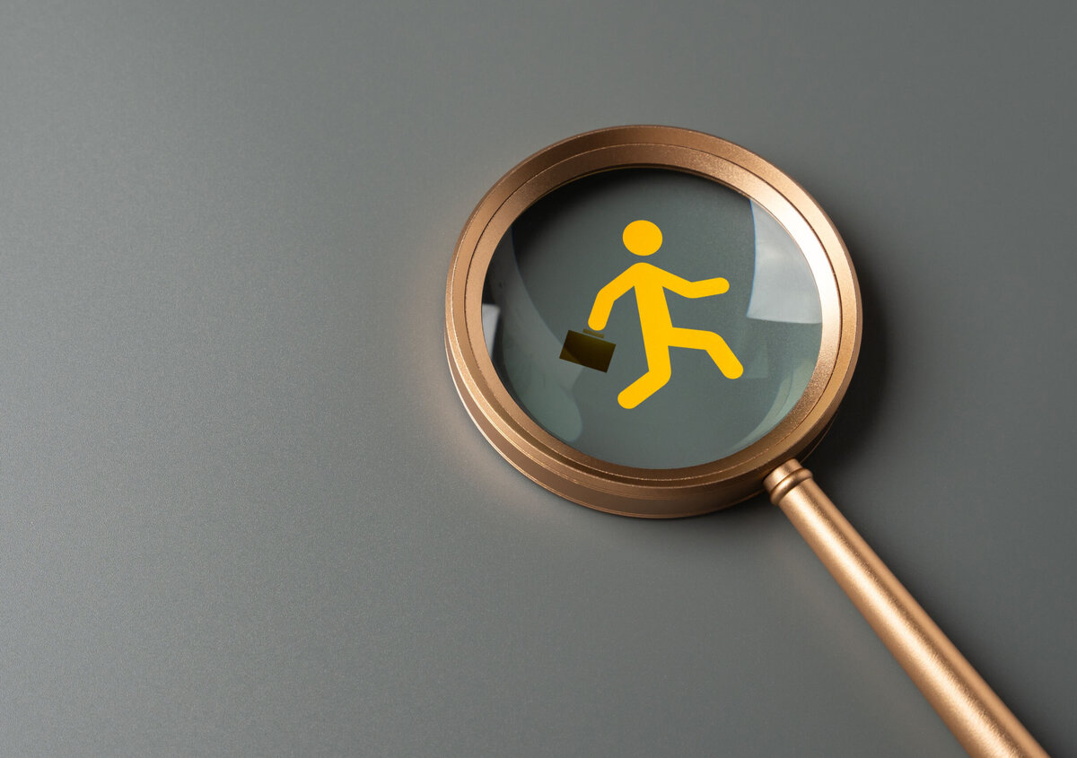 Goldfarbene Lupe auf grauem Hintergrund. Im Vergr&ouml;&szlig;erungsglas ist ein gelbes Symbol einer gehenden Person mit Aktentasche dargestellt. Die Illustration symbolisiert die Suche nach Fachkr&auml;ften, Personalgewinnung oder den Umgang mit Fachkr&auml;ftemangel. Der linke Bildbereich bietet ausreichend Freiraum f&uuml;r &Uuml;berschriften oder weitere Inhalte.