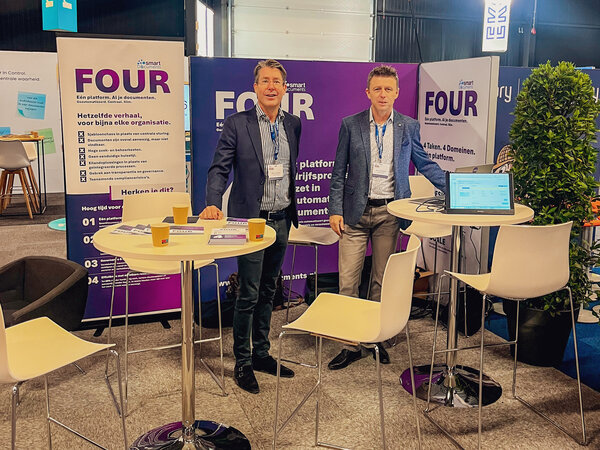 Bild vergr&ouml;&szlig;ern: SmartDocuments presenteert het documentplatform FOUR op CorporatiePlein 2026. Twee medewerkers staan voor banners en een softwaredemo op de beursstand.