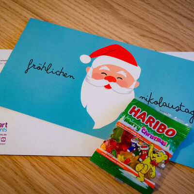 Bild vergr&ouml;&szlig;ern: Aufnahme Voderseite: Nikolausmailing f&uuml;r Teilnehmer:innen des Webinars "Zusatzmodule Serienbriefe + E-Mail-Plugin". Fotografie Schreibtisch mit Briefumschlag und Mailing sowie einer T&uuml;te Haribo.